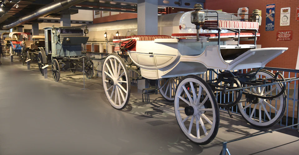 Vintage white carriages with large wheels and striped red-and-white seats on display in a museum setting.