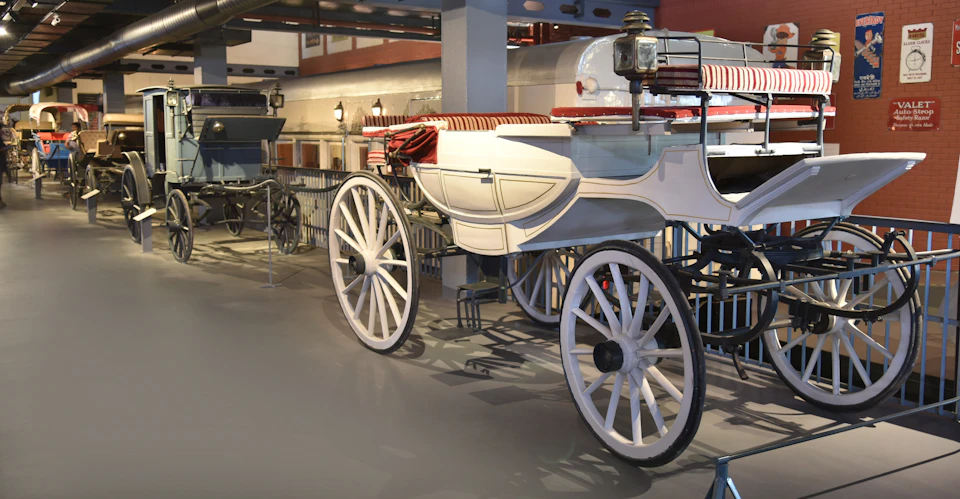 Vintage white carriages with large wheels and striped red-and-white seats on display in a museum setting.