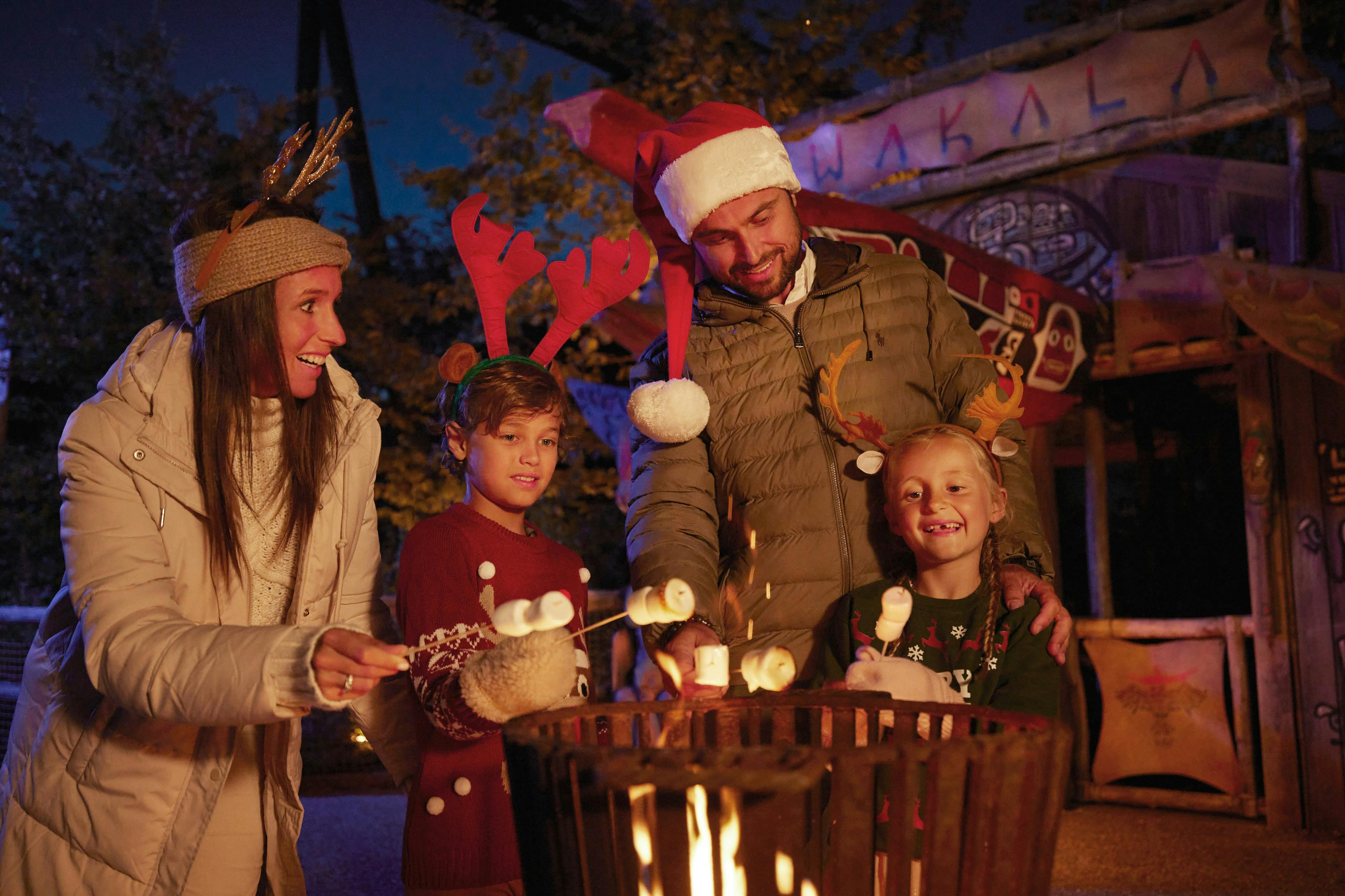 A family wearing festive attire toasts marshmallows over a fire pit during an outdoor evening gathering.