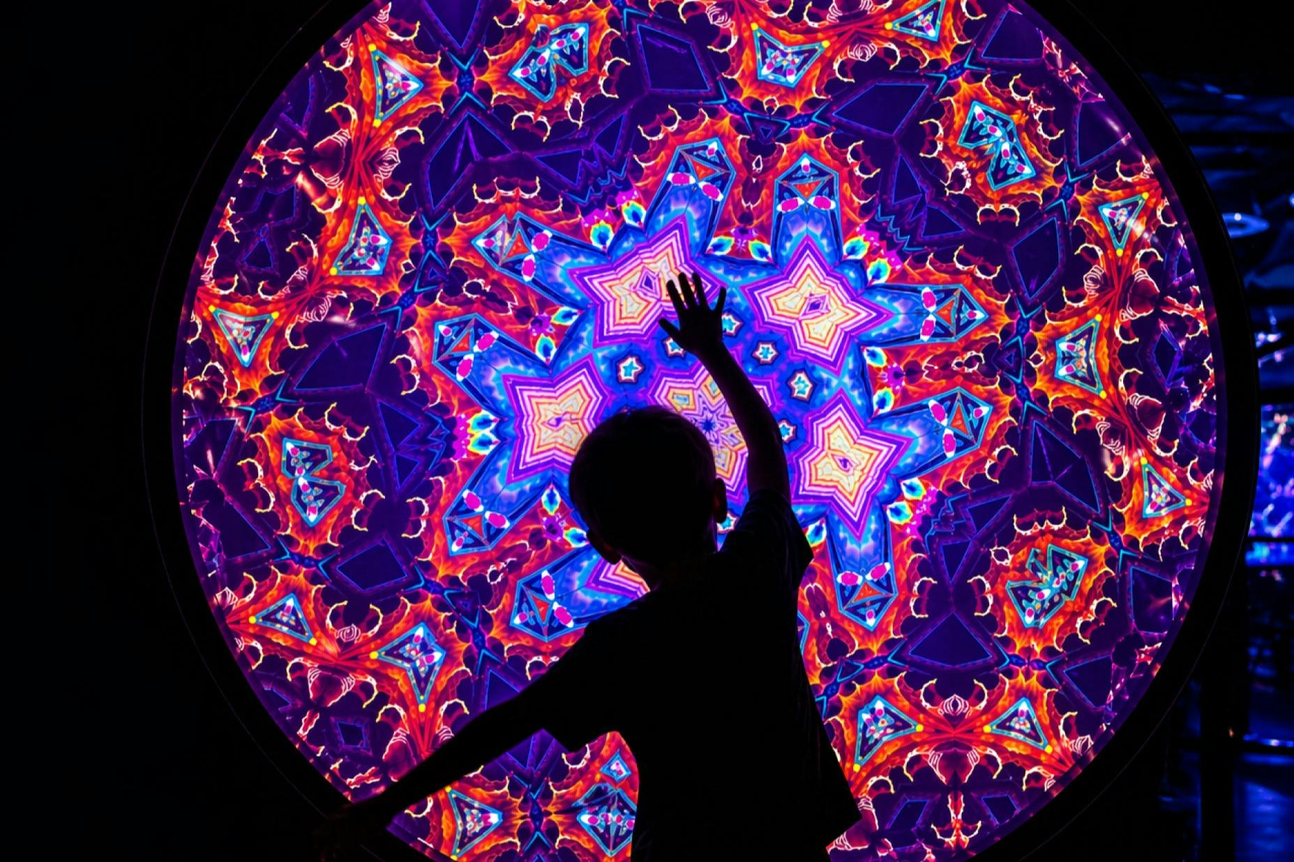 A silhouette of a child reaching toward a vibrant kaleidoscopic pattern featuring colorful geometric shapes.