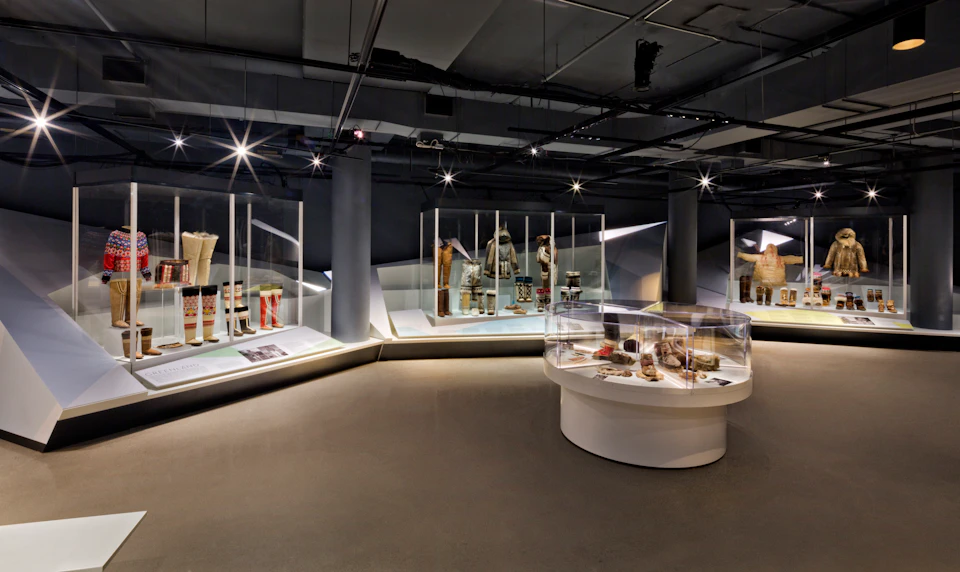 A modern museum exhibit featuring clothing and accessories displayed in glass cases under soft lighting.