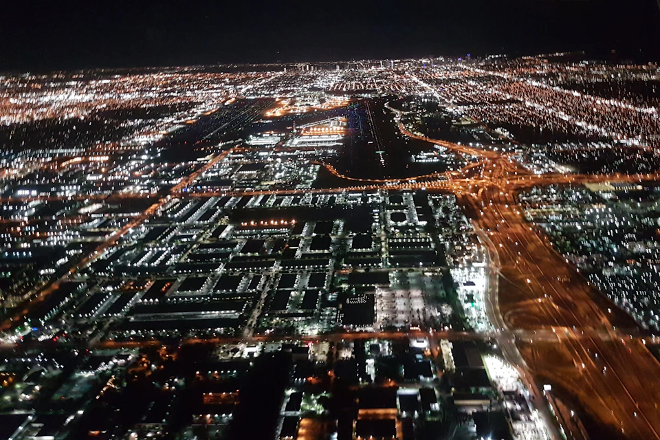 Aerial nighttime view of a cityscape with illuminated streets, buildings, and highways.