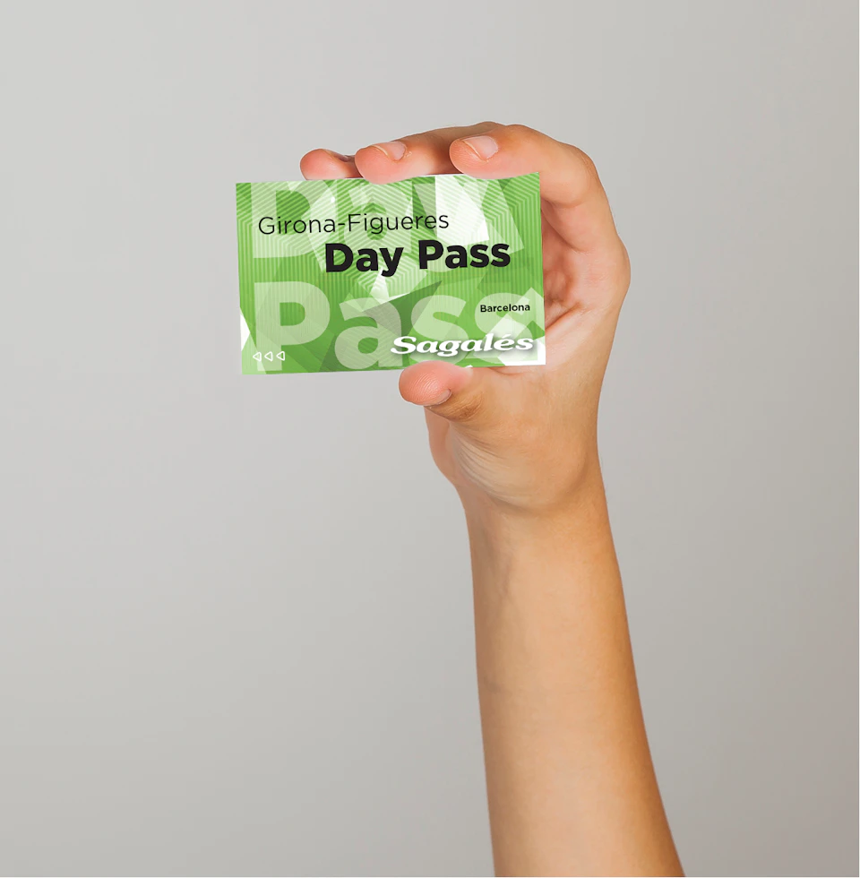 A hand holding a green day pass ticket reading "Girona - Figueres Day Pass, Sagalés, Barcelona" against a plain background.
