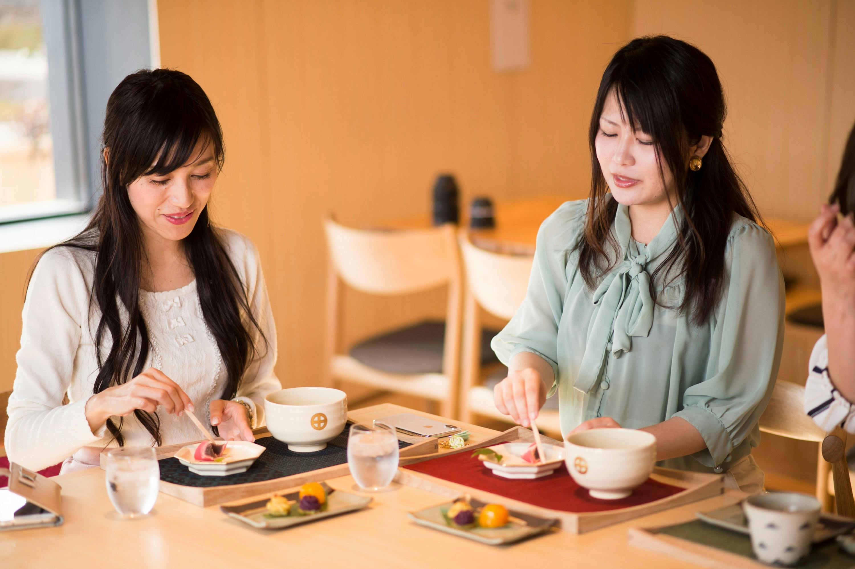 Two women enjoying a meal with tea in a brightly lit restaurant, seated at a wooden table with elegant dishware.