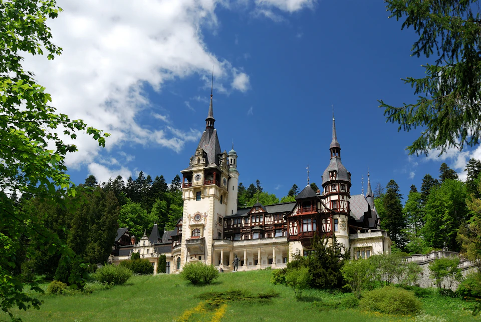 Ornate castle with tall spires and intricate woodwork set against a clear blue sky and surrounded by lush greenery.