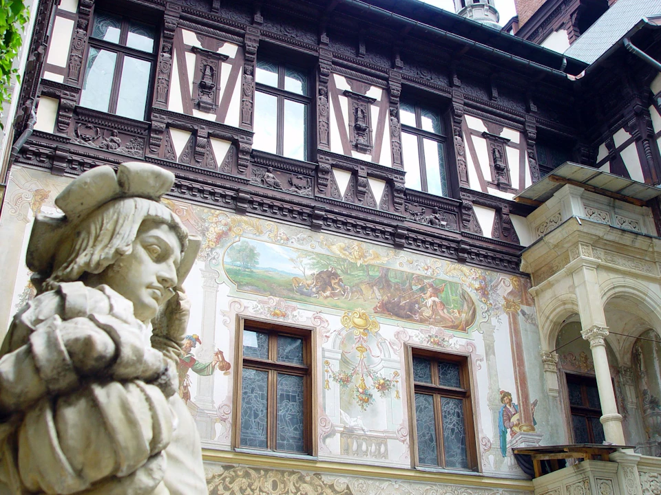 Historic building facade with intricate woodwork, detailed murals, and a stone statue in the foreground.