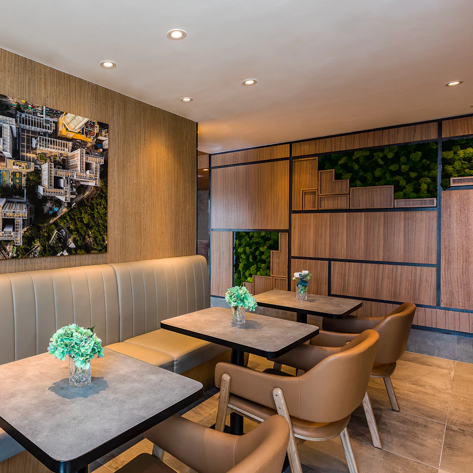 Modern café with beige banquette seating, brown chairs, and two tables. Aerial city photo on the wall and green plants in decor.