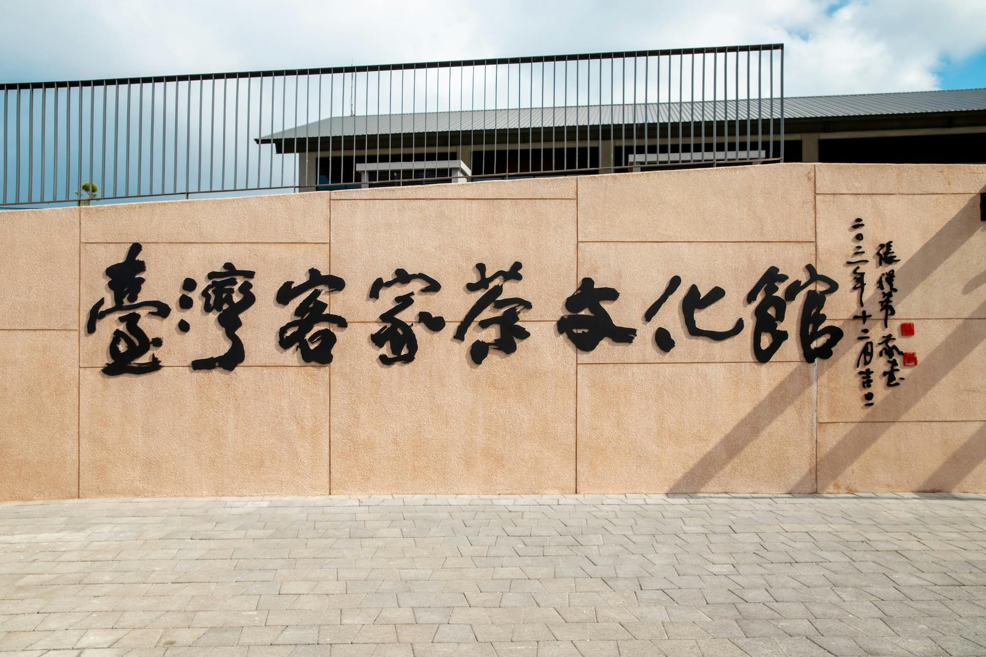 A beige wall with black Chinese characters displayed prominently, in front of a modern building with a fenced roof.