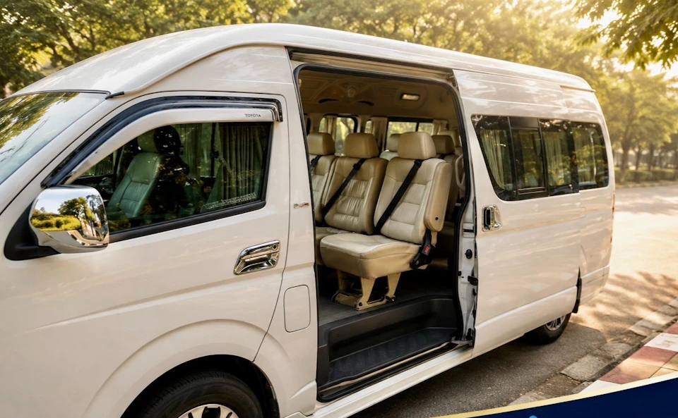 A white passenger van with its sliding door open, showing beige leather seats inside. The van is parked outdoors.