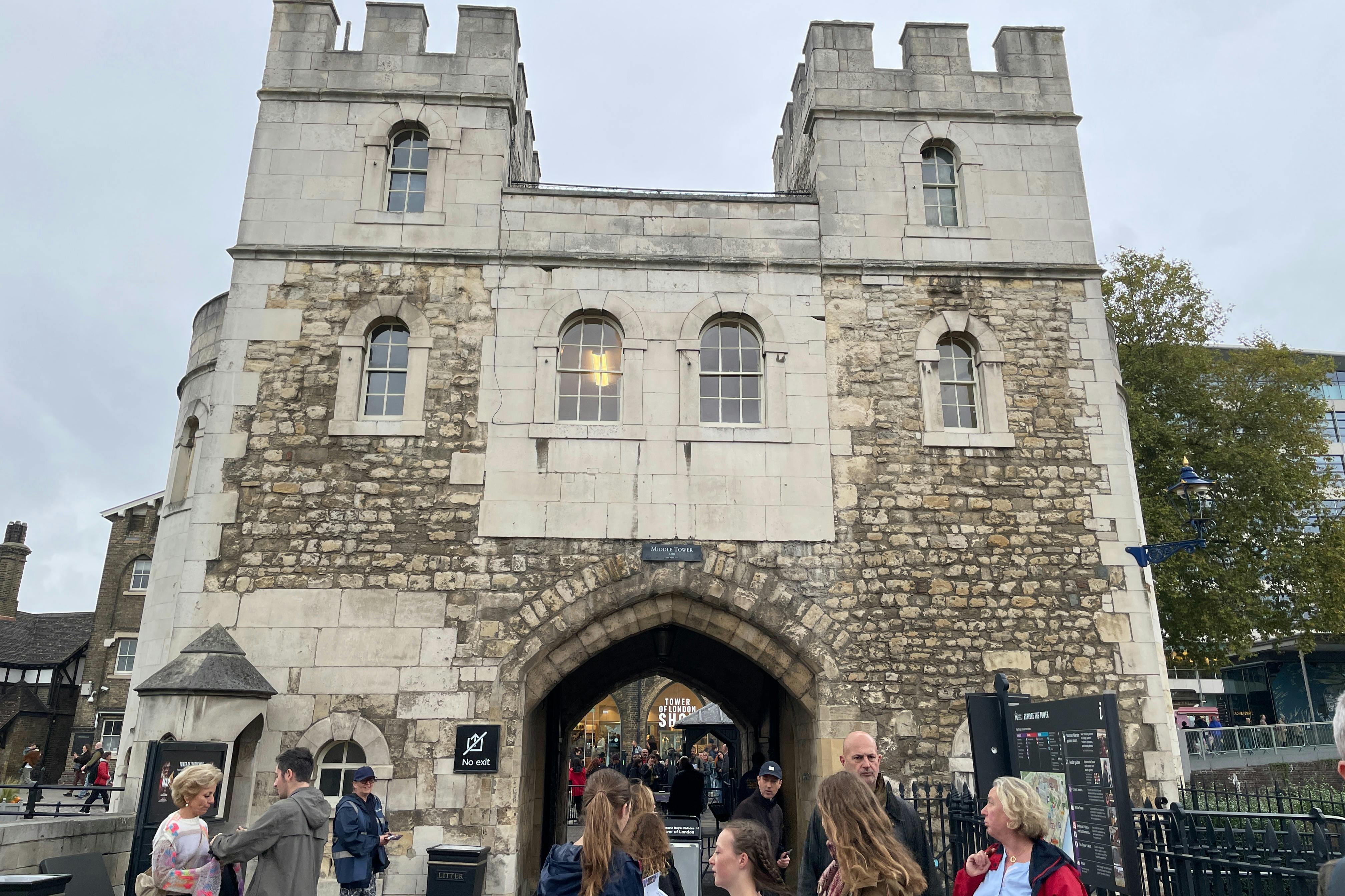 Вход в каменную арку с людьми, собравшимися снаружи. На табличке написано «На пристань». На заднем плане видны деревья и магазины.