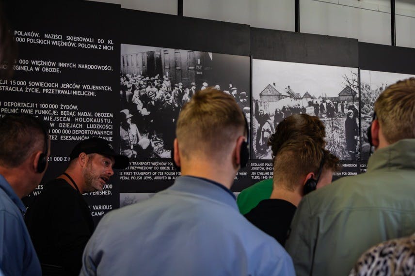 一群人在博物馆里观看带有照片和文本的历史展览。 显示屏上的文字为波兰语。