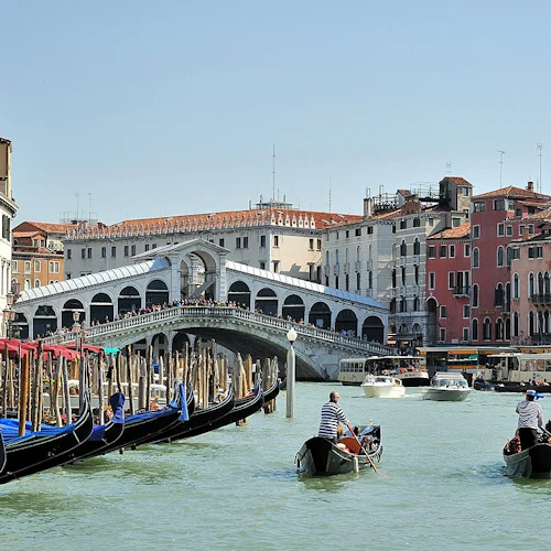 Gondoler på en kanal i Venedig med Rialtobron i bakgrunden och färgglada byggnader längs vattenvägen.