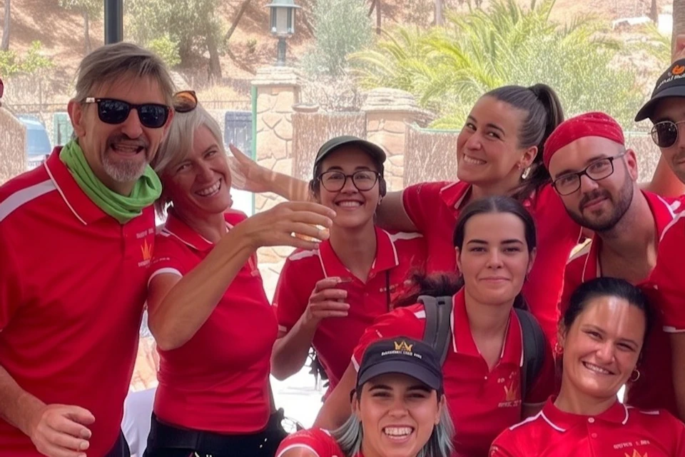 A group of people wearing red shirts posing together outdoors, smiling and making positive gestures in the shade.