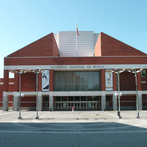 Modern tegelbyggnad med "Auditorio Nacional de Música" -skyltar, stora pelare, banderoller och en plaza. Få människor är i sikte.