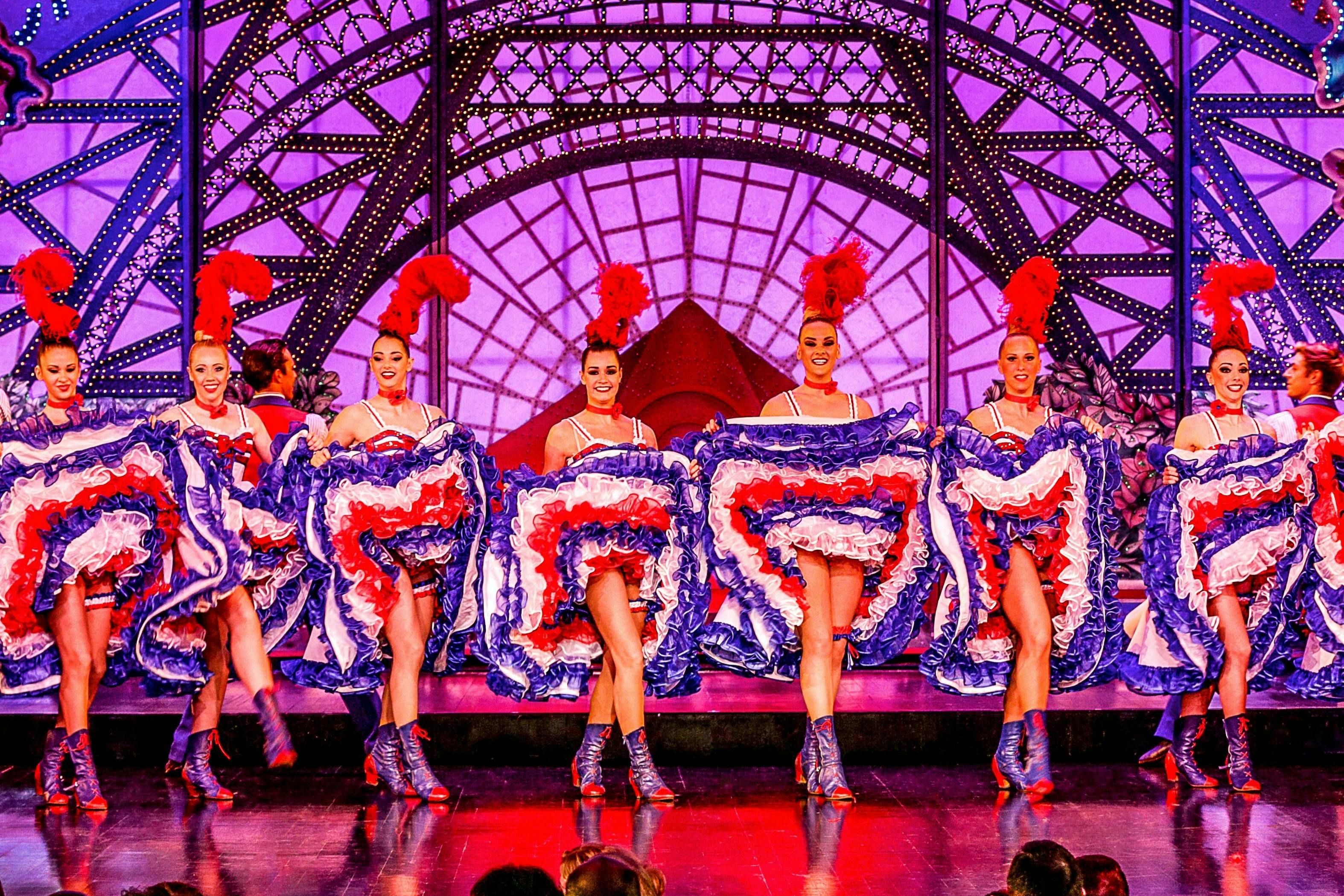 Des artistes en costumes colorés, dansant et brandissant des jupes à volants, sur une scène brillamment éclairée avec une toile de fond ornée.