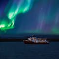 Una barca rossa e bianca che naviga nella baia di Faxaflói sotto l'aurora boreale.