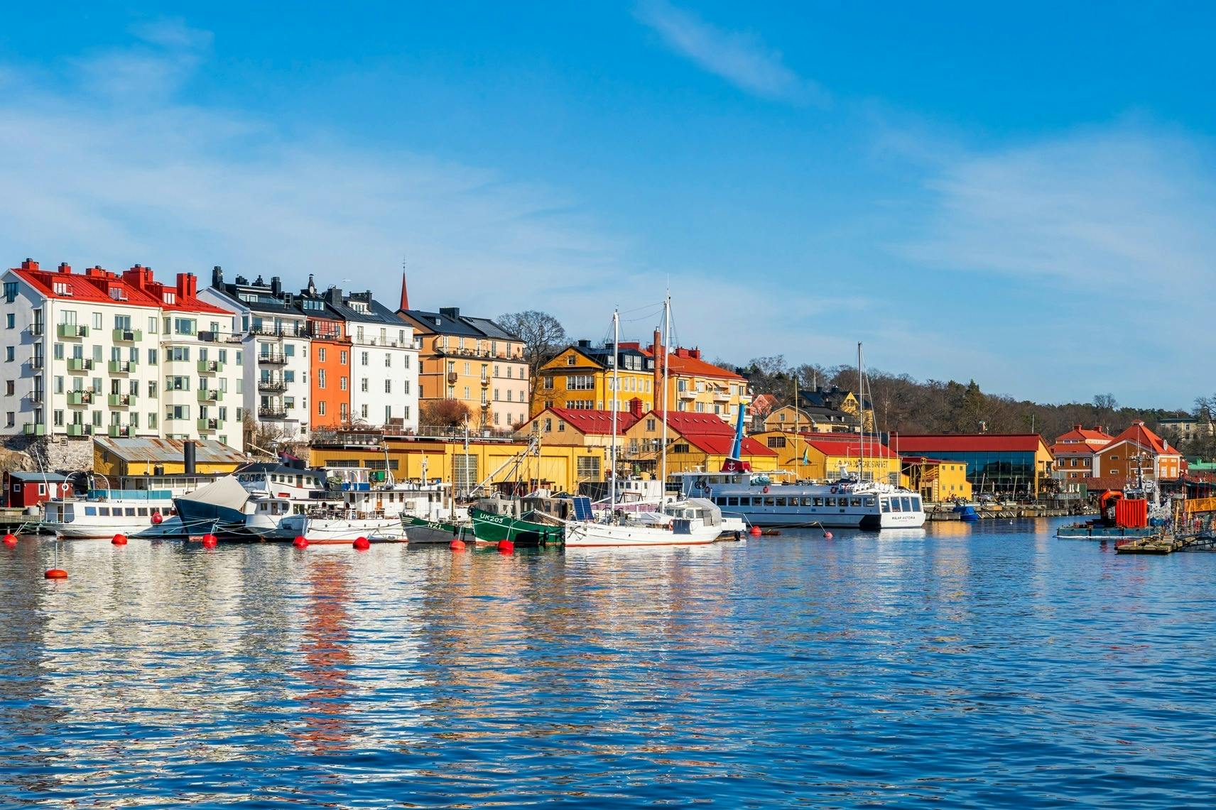 Colorful buildings and boats line a calm waterfront under a blue sky.
