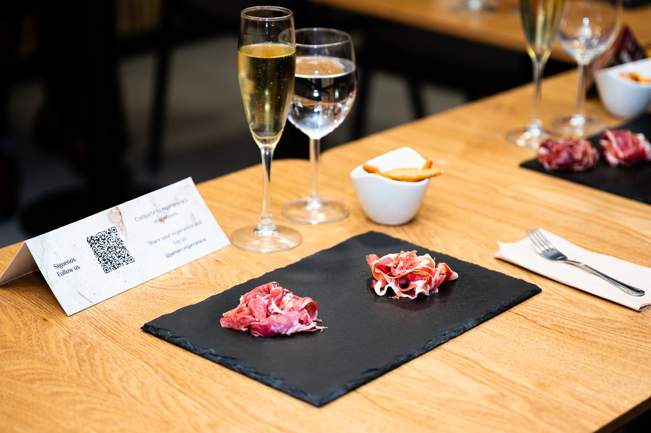 Um prato de ardósia preta com duas porções de carne curada, um copo de champanhe, um copo de água e uma pequena taça com pãezinhos.