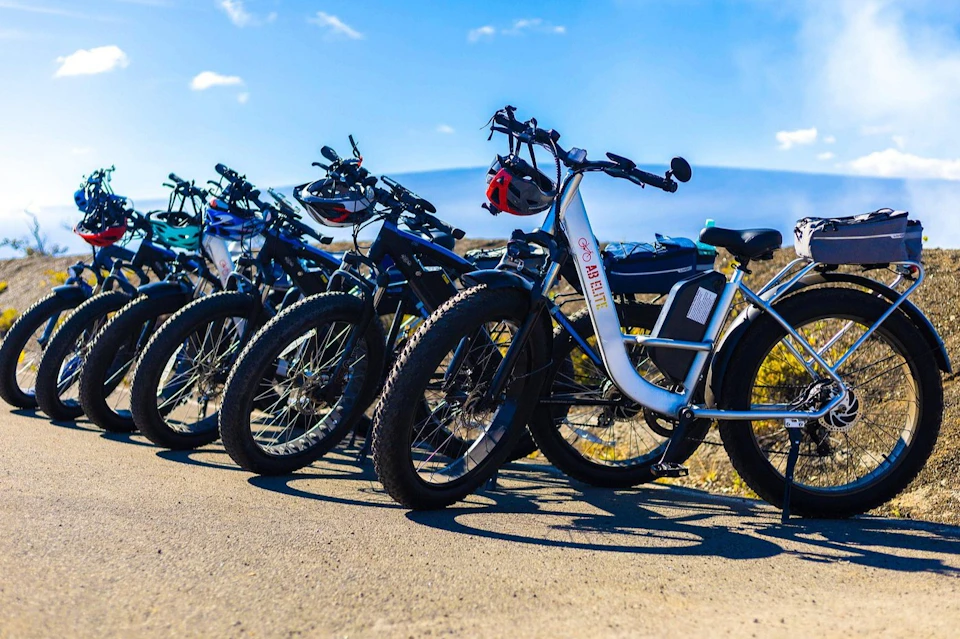 Four electric bikes with large tires parked on a paved surface under a clear blue sky.