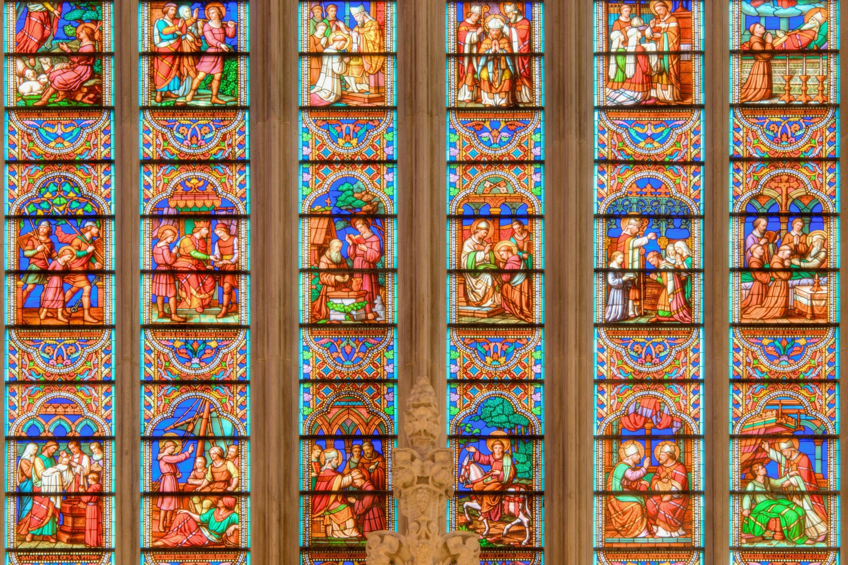 Colorful stained glass windows in a cathedral, depicting various religious scenes and figures, with intricate designs.