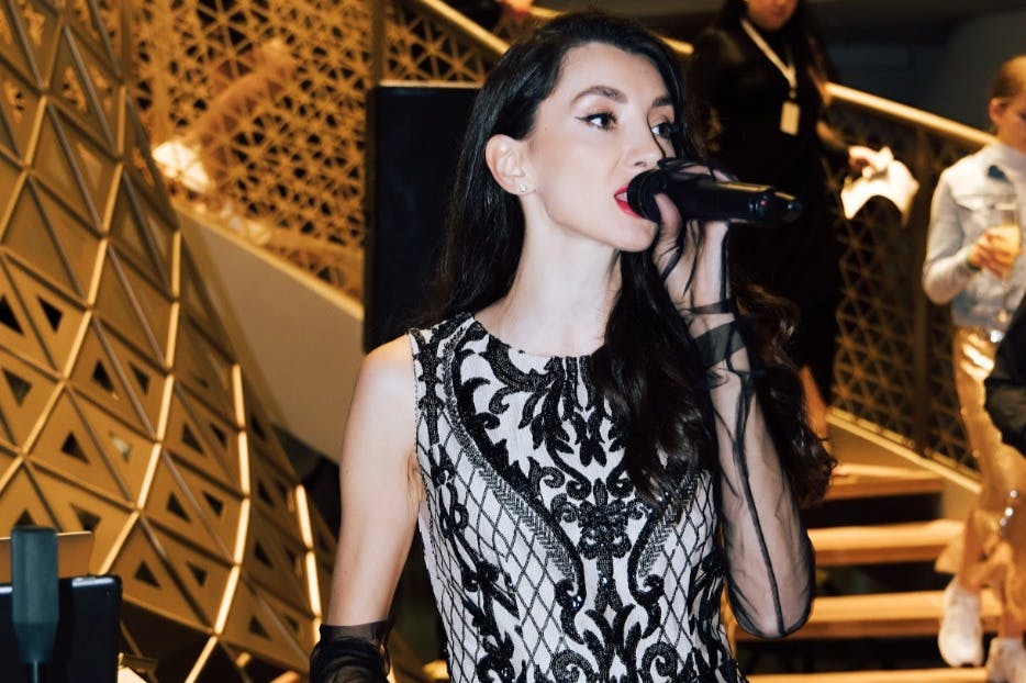 一位女士穿着精致的黑白连衣裙，戴着纯手套，在时尚的室内环境中对着麦克风唱歌。