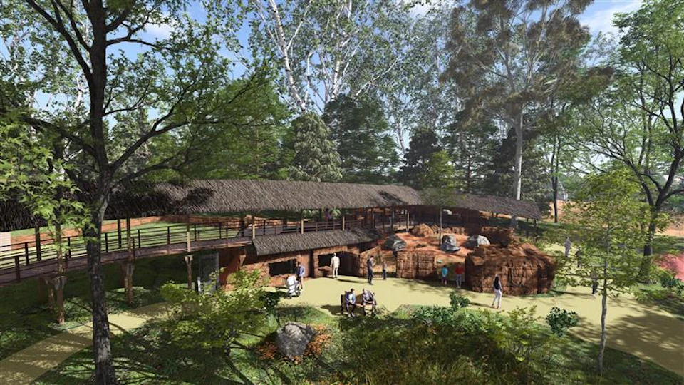 A park scene with people walking and sitting near a thatched-roof structure surrounded by trees and rocks.