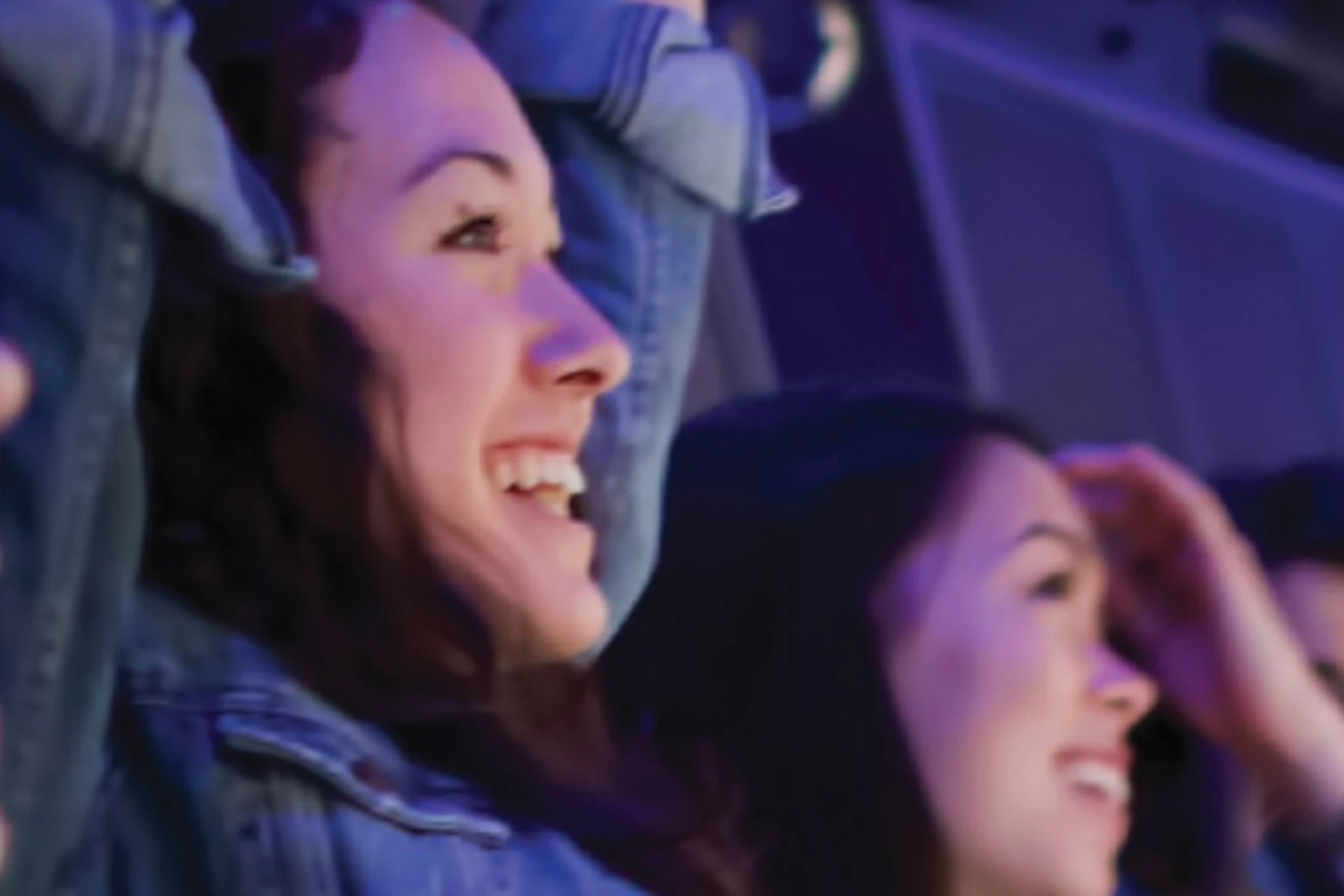 People seated in a flight-simulator-like ride, raising their arms and enjoying a scenic view of the ocean and coastline.