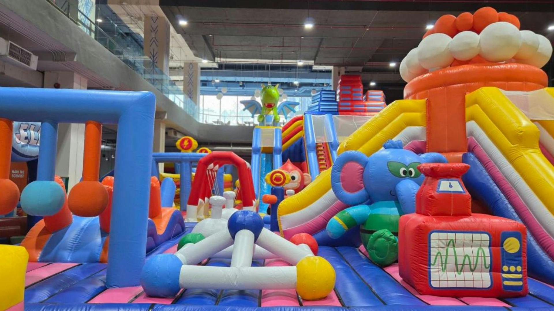 Zona de joc inflable interior amb tobogans de colors, estructures i decoracions amb temàtica animal sota un sostre alt.