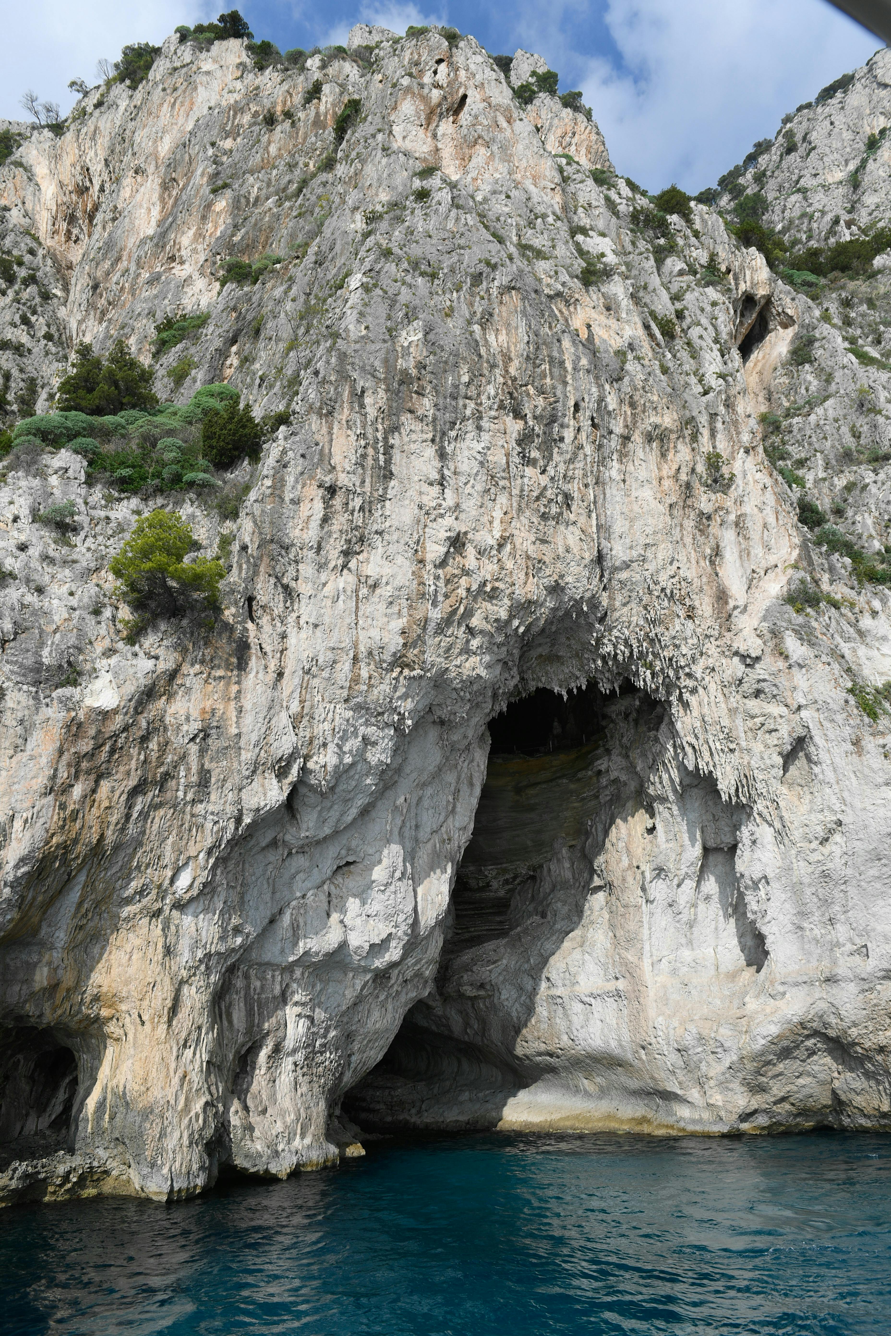 崖の上の緑に囲まれた、目立つ洞窟の開口部を持つ大きな岩層。