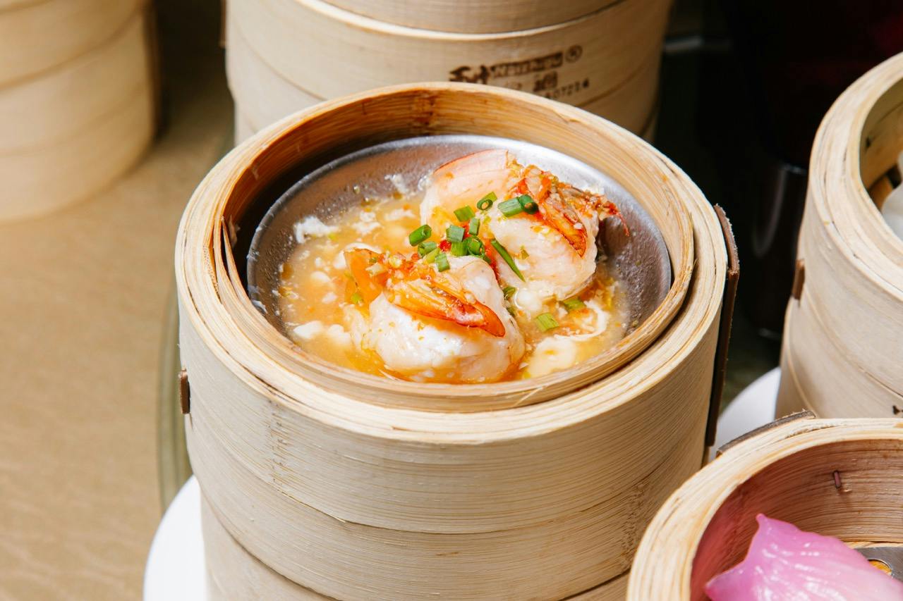 A bamboo steamer containing a dish with seafood, garnished with green onions and sauce.