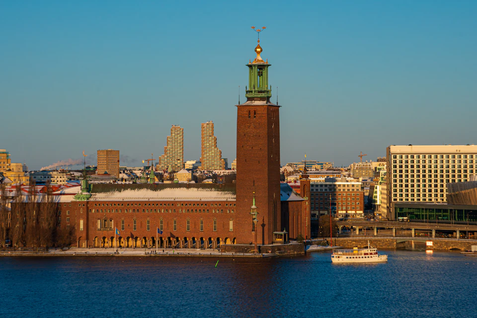 A view of Stockholm City Hall by the water, with a boat nearby and modern buildings in the background.
