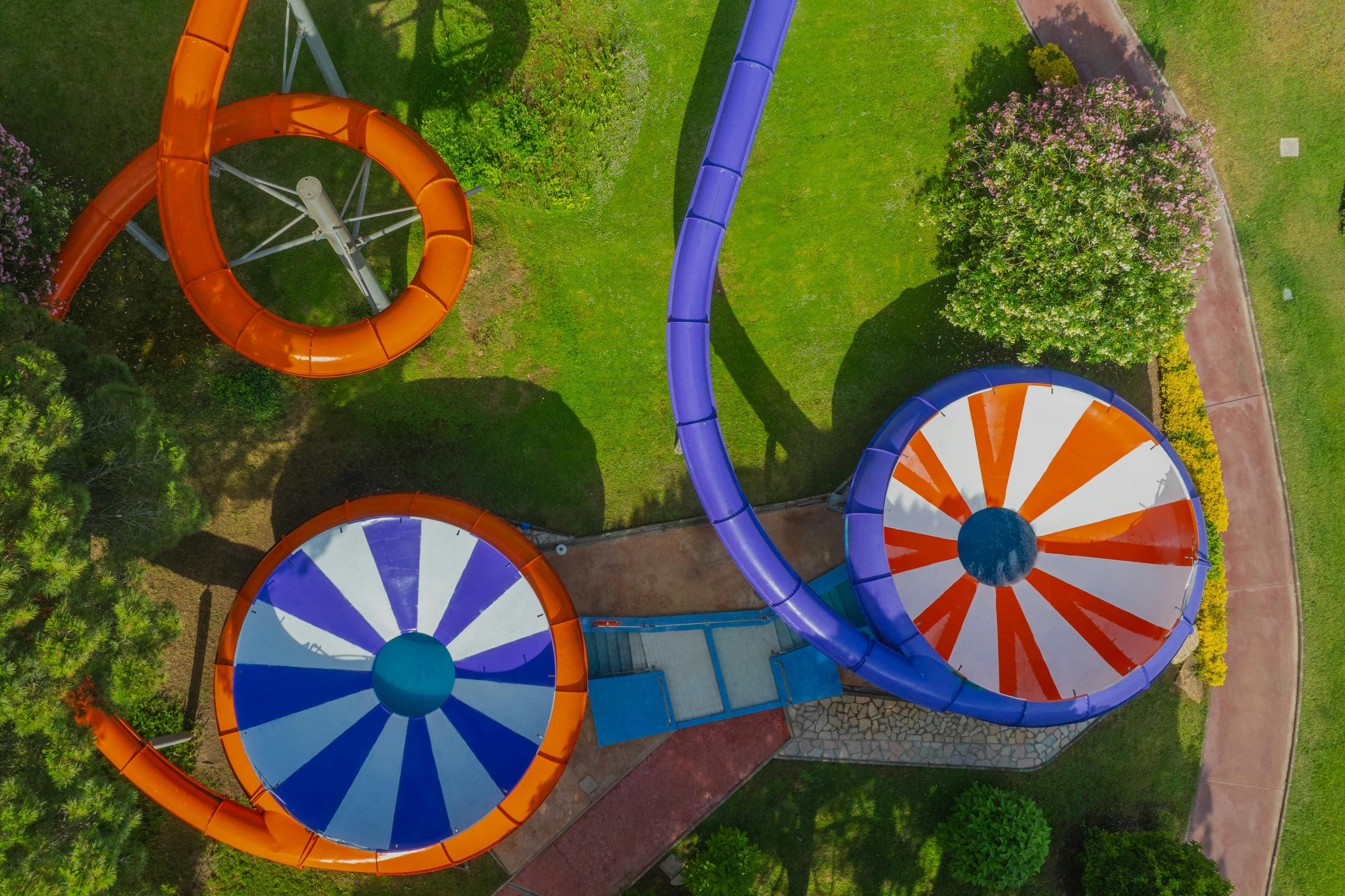 Vista aérea de escorregas aquáticos coloridos e funis num parque de diversões rodeado de relva e caminhos.