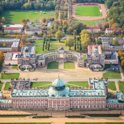 Aerial view of a large baroque palace with a green dome, courtyards, and surrounding formal gardens and buildings.