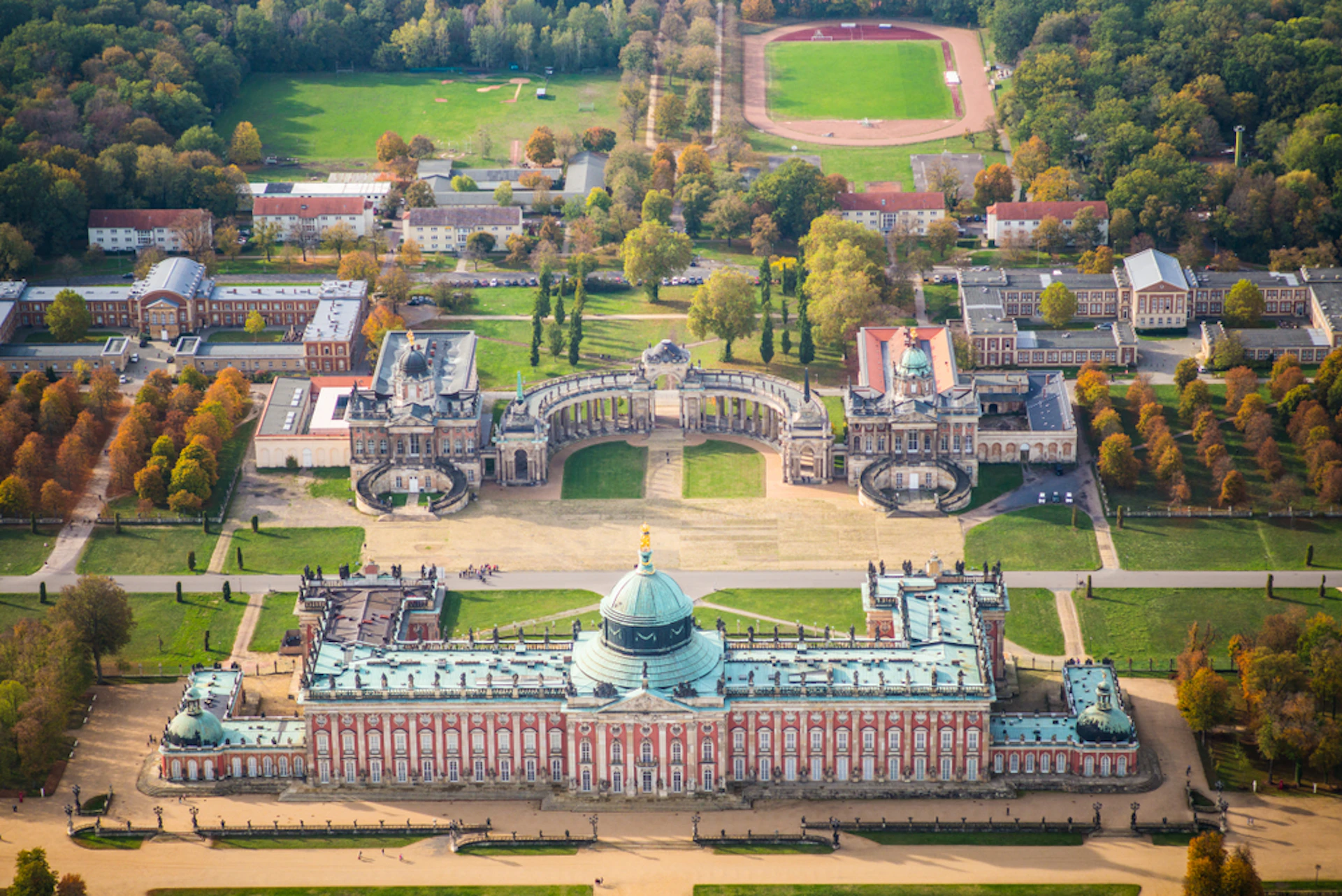 Aerial view of a large baroque palace with a green dome, courtyards, and surrounding formal gardens and buildings.