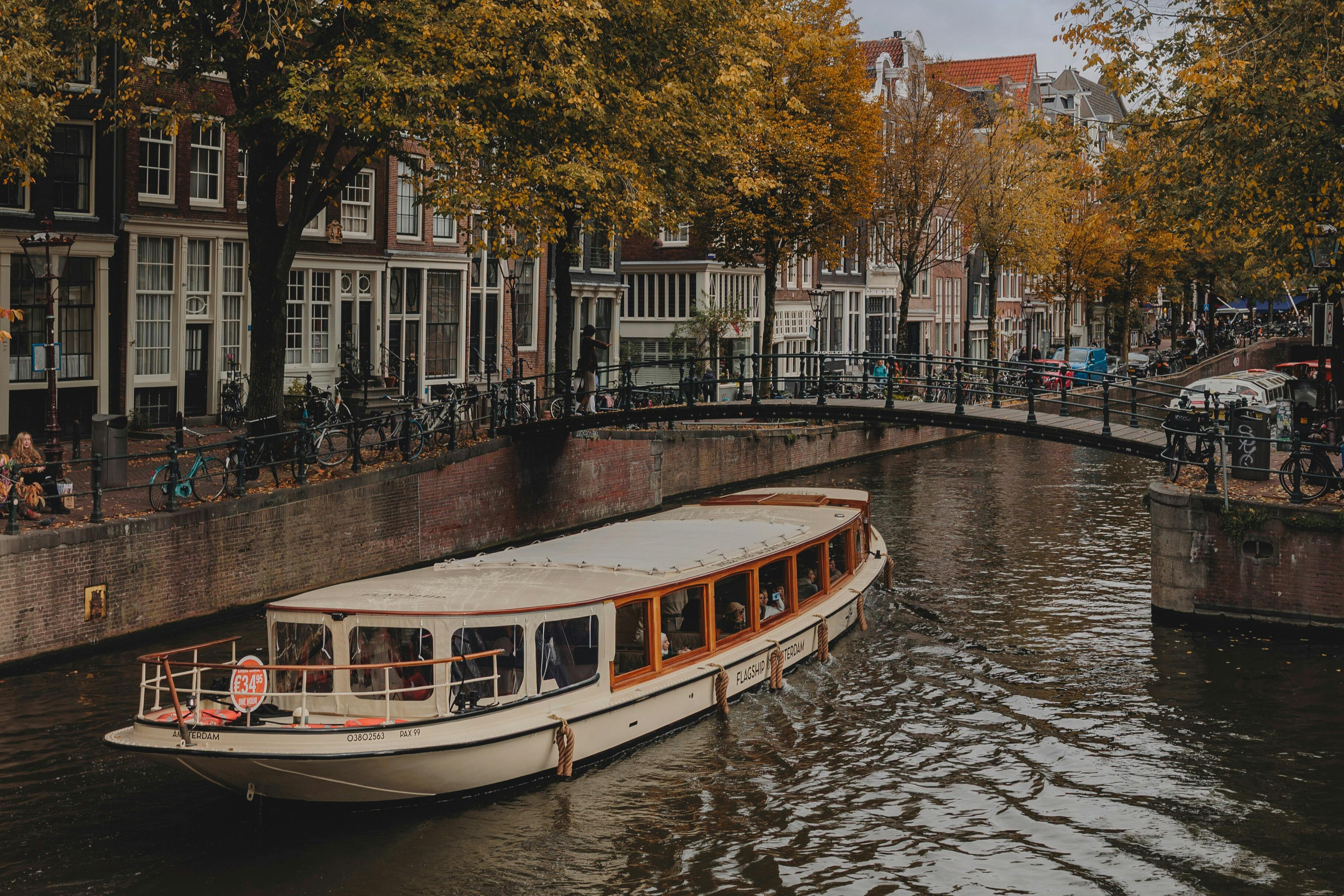 Boot vaart door een kanaal met bomen en historische gebouwen. Fietsen rusten op een reling erboven.