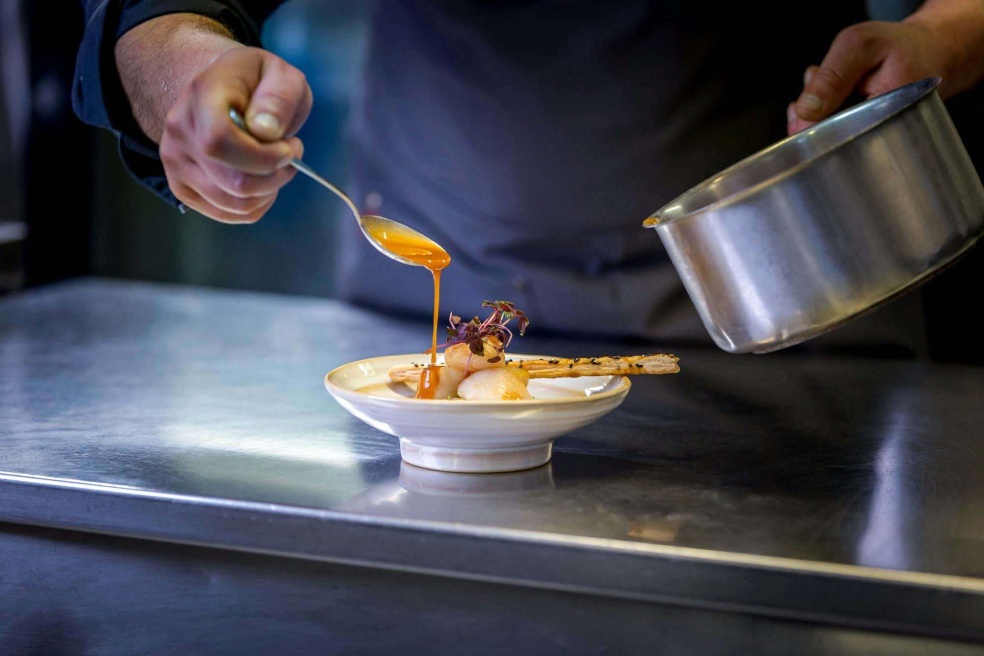 Eine Person träufelt Sauce auf einen Gourmet-Teller auf einem Edelstahltisch.