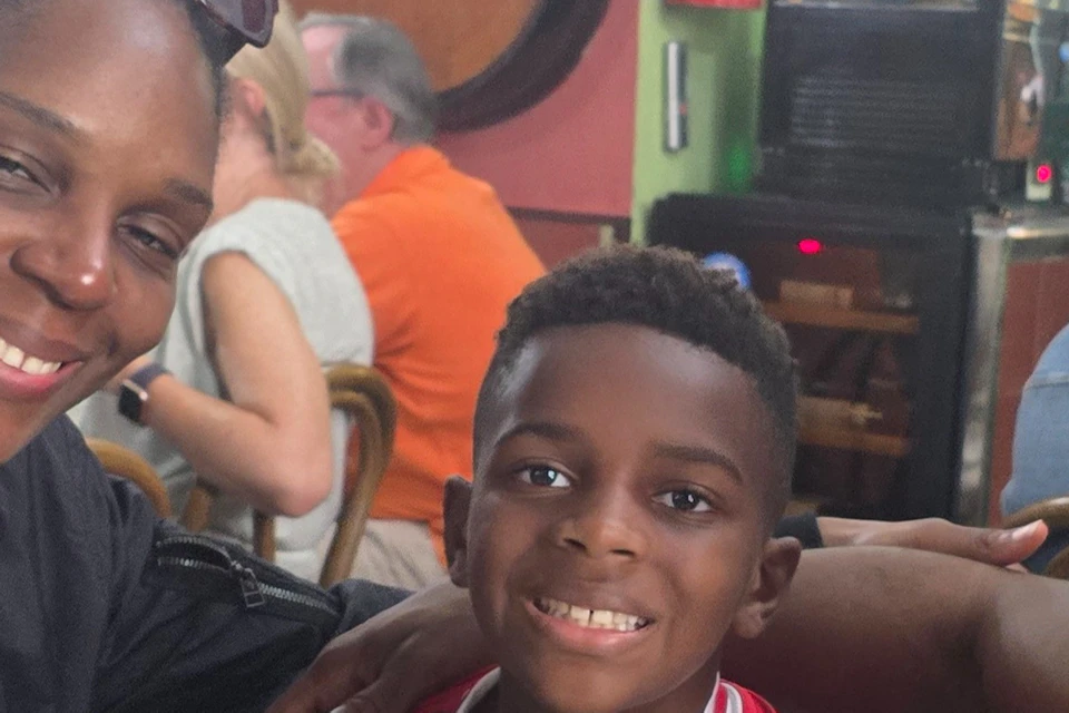 Three people smiling at a table in a colorful restaurant. Food and drinks are on the table; the child is wearing a red sports jersey.