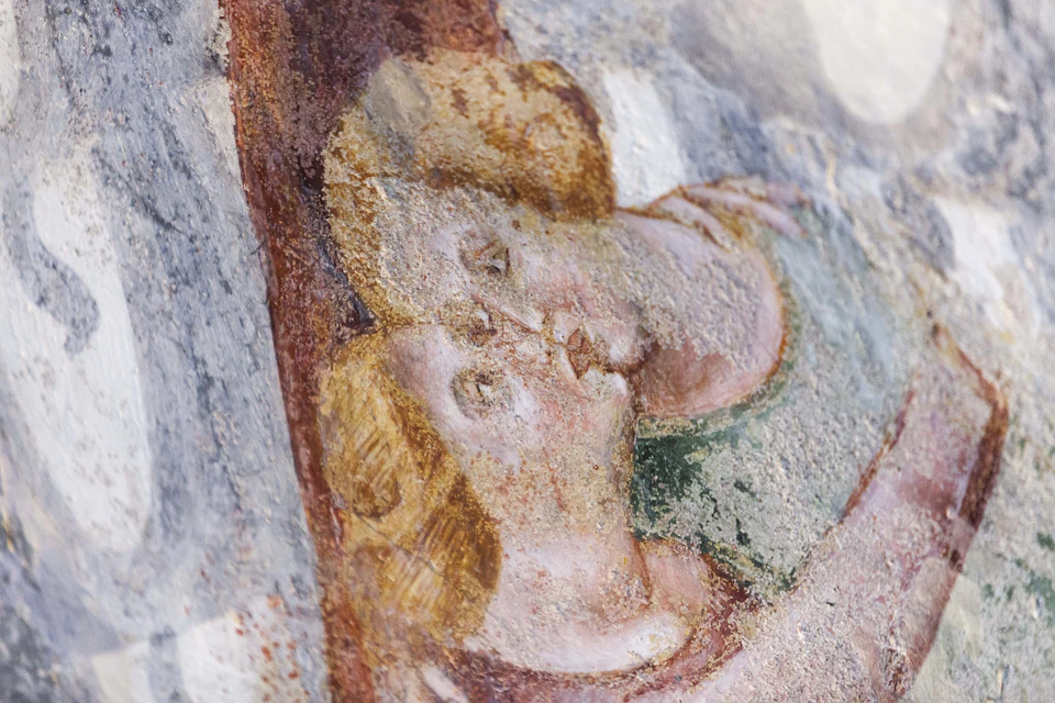 A faded fresco depicts two faces with long hair and closed eyes, embracing or kissing. The artwork shows signs of age and erosion.