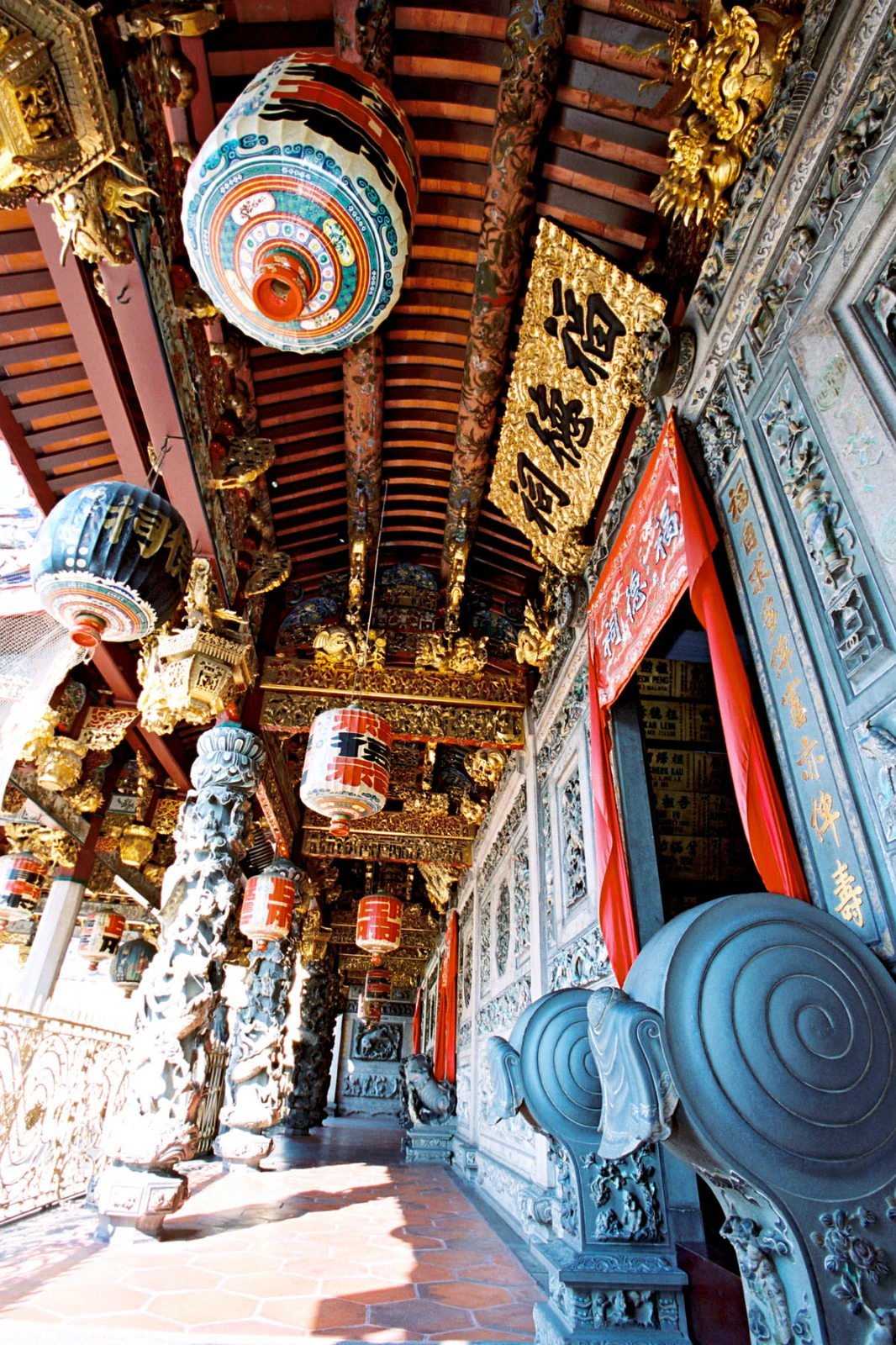 Ornate temple interior with carved stone pillars, hanging lanterns, and intricate golden decorations.
