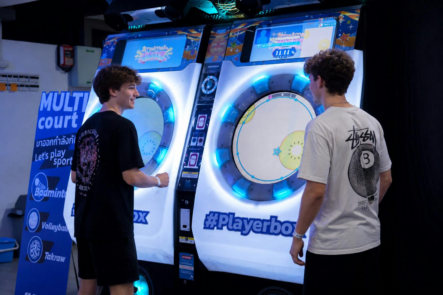 A young man interacts with a lit-up arcade game machine in a recreational area with a sign advertising sports activities nearby.