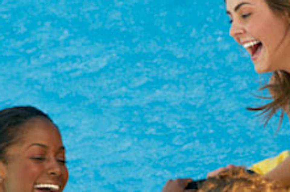 Three people in swimsuits are laughing and enjoying a ride on a yellow inflatable raft in a pool.
