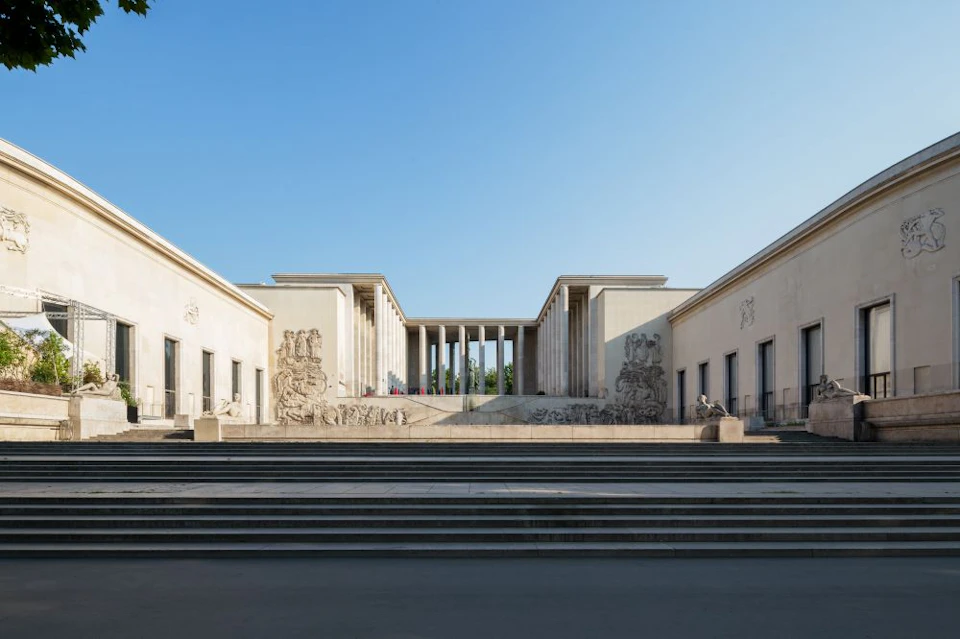 A neoclassical building with columns, decorative carvings, and a wide staircase under a clear blue sky.