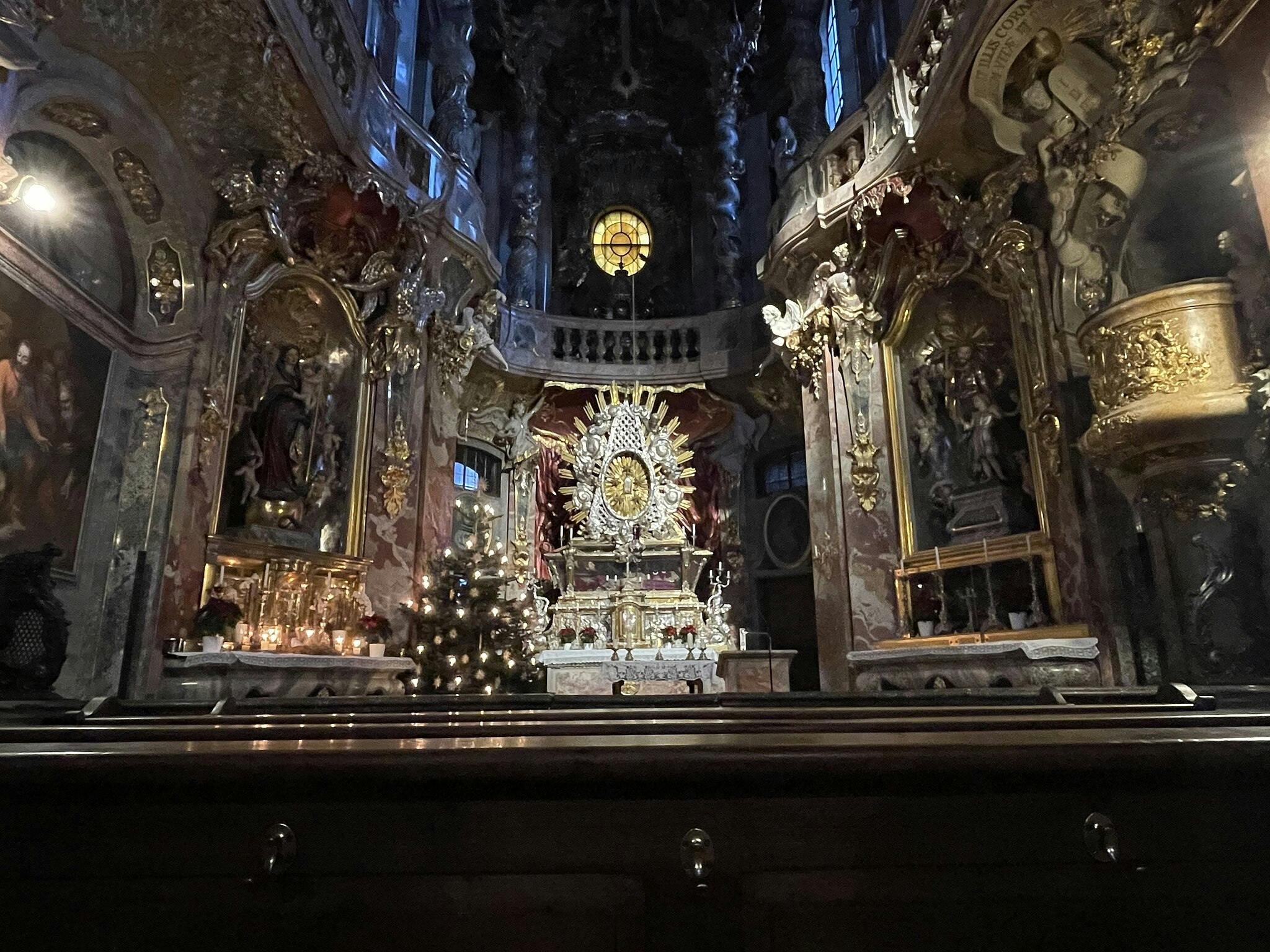 華やかな金色の装飾、複雑な彫像、クリスマスツリーを備えたエレガントな教会の内部。 中央にはロウソクで照らされた祭壇があります。