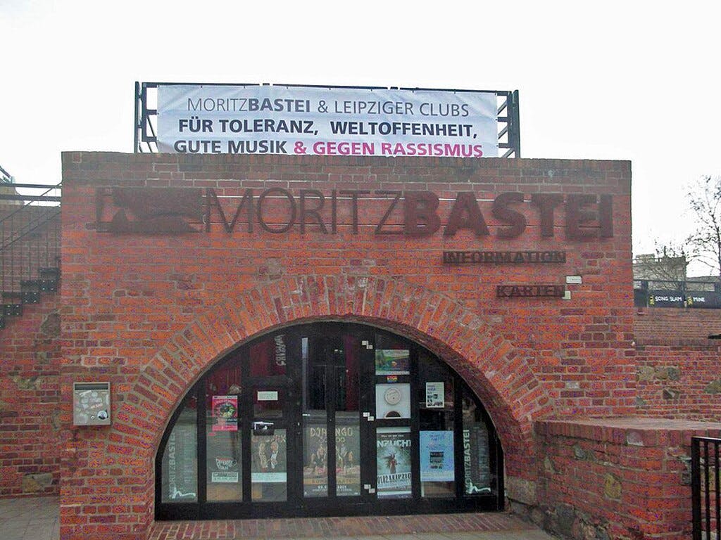 Brick entrance of Moritzbastei with arched doorway and signs promoting tolerance, worldliness, good music, and opposing racism.