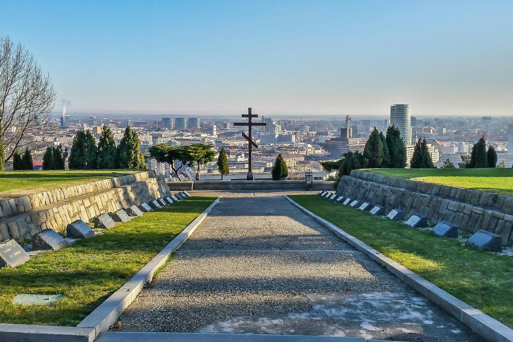 通往大十字架的小径，背景是城市景观，周围环绕着绿色植物和墓碑。