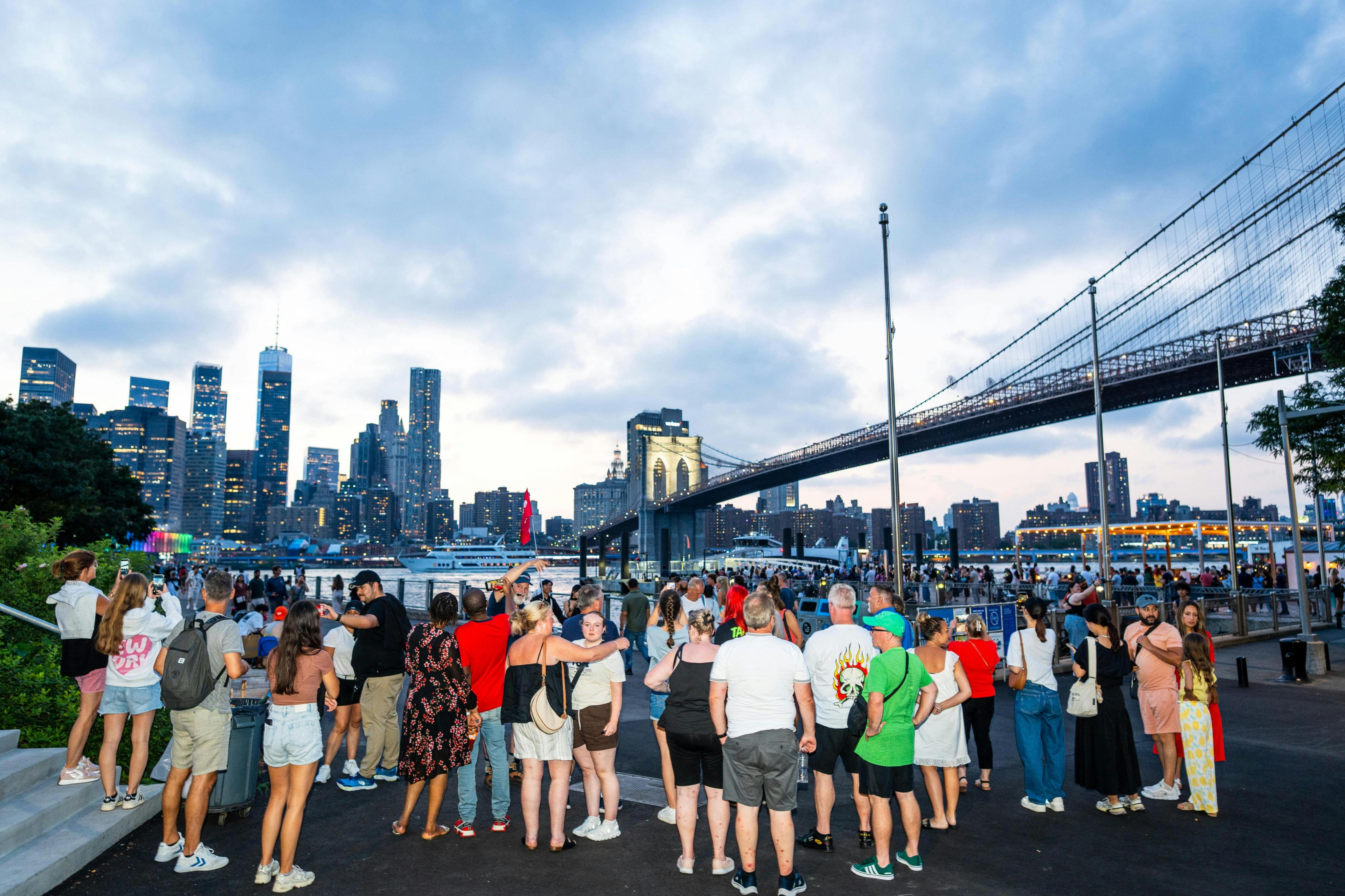 해질 무렵 브루클린 브리지와 뉴욕 스카이라인을 배경으로 수많은 사람들이 물가에 모여듭니다.