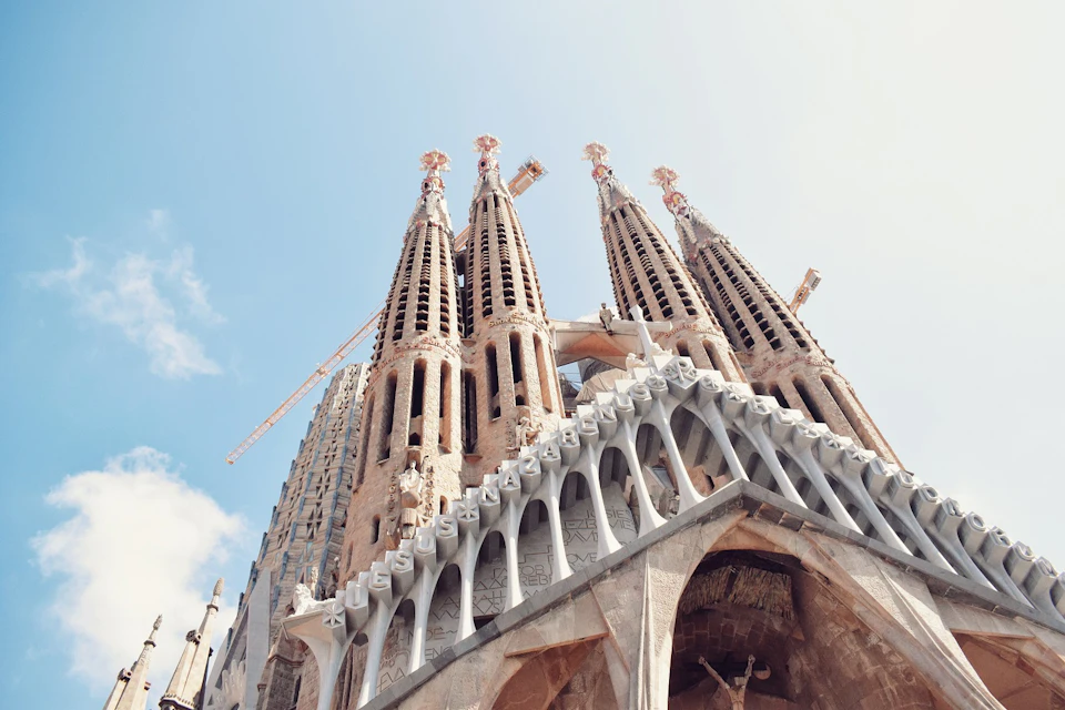 Close-up view of Sagrada Familia's ornate towers against a clear sky. Construction cranes are visible in the background.