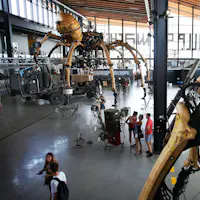 Des personnes à l'intérieur d'un grand entrepôt moderne avec une araignée robotique géante et diverses expositions mécaniques.
