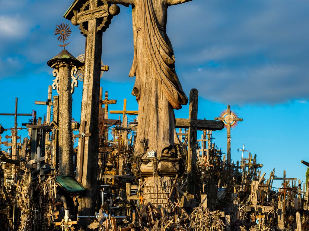 Liczne drewniane krzyże o różnych rozmiarach otaczają centralny posąg Chrystusa na tle błękitnego nieba.