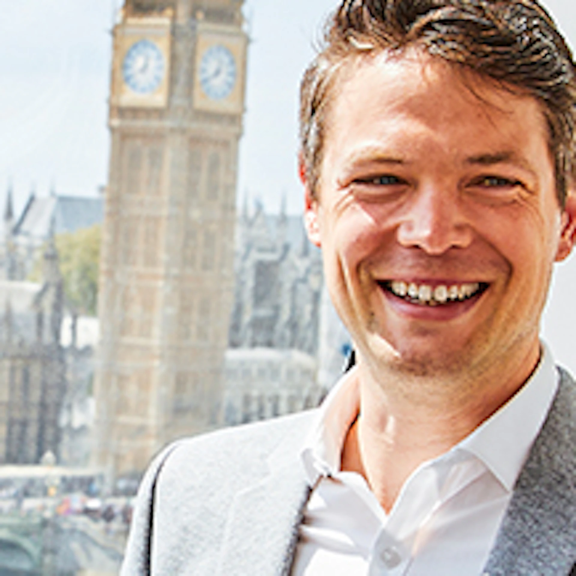 Three people smiling and talking inside a London Eye capsule with Big Ben and the Houses of Parliament visible in the background.